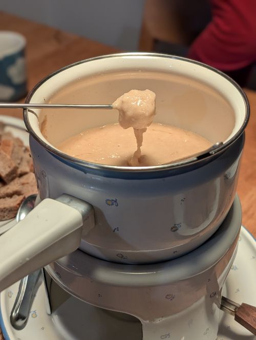 Ein Stück Brot auf einem Spieß von dem etwas Käse zurück in den Fonduetopf tropft
