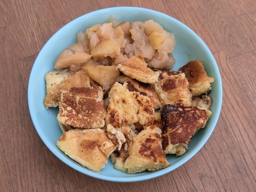 Eine Portion Kaiserschmarrn mit gekochten Apfelstücken in einer blauen Schüssel auf einem Holztisch