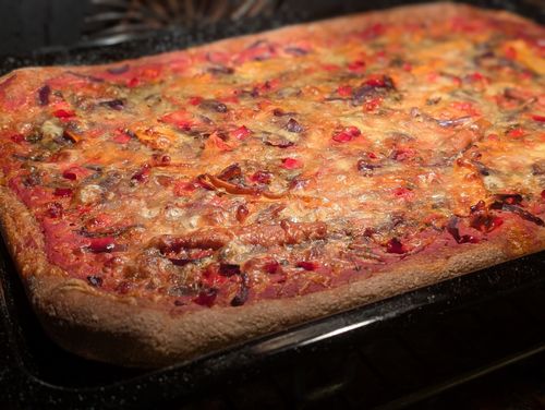 Fertig gebackene rechteckige Pizza auf einem Blech im Backrohr